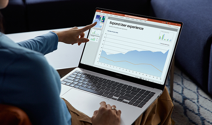 'O Galaxy Book4 Pro cinza está aberto com uma apresentação aberta no aplicativo Microsoft PowerPoint na tela e o dedo de uma pessoa tocando na tela sensível ao toque.