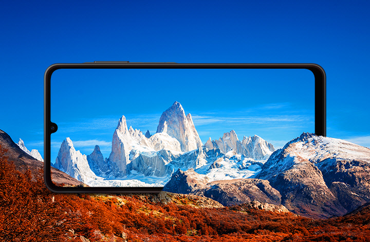 Um Galaxy A06 5G é posicionado horizontalmente entre montanhas rochosas. A tela enquadra montanhas com neve ao fundo contra um céu azul.